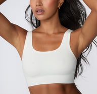 On a light studio backdrop, a close-up front view shows a model wearing the Ribbed Scoop Bralette in White, highlighting the scoop neckline, soft ribbed fabric, and wide straps.
