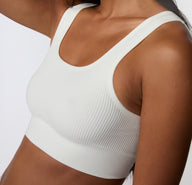 On a light studio backdrop, a close-up angled view shows a model wearing the Ribbed Scoop Bralette in White, focusing on the ribbed texture, smooth underband, and wireless design.