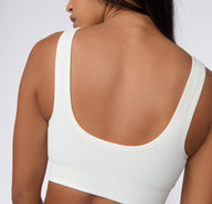 On a light studio backdrop, a back view shows a model wearing the Ribbed Scoop Bralette in White, highlighting the scoop back shape, wide straps, and smooth ribbed fabric.