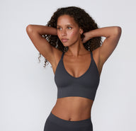On a light studio backdrop, a mid-length front view shows a model wearing the Ribbed Triangle Bralette in Charcoal, emphasizing the triangle shape, ribbed texture, and wireless design.