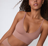 On a light studio backdrop, a close-up angled front view shows a model wearing the Ribbed Triangle Bralette in Plum, highlighting the triangle neckline, soft ribbed fabric, and thin straps.