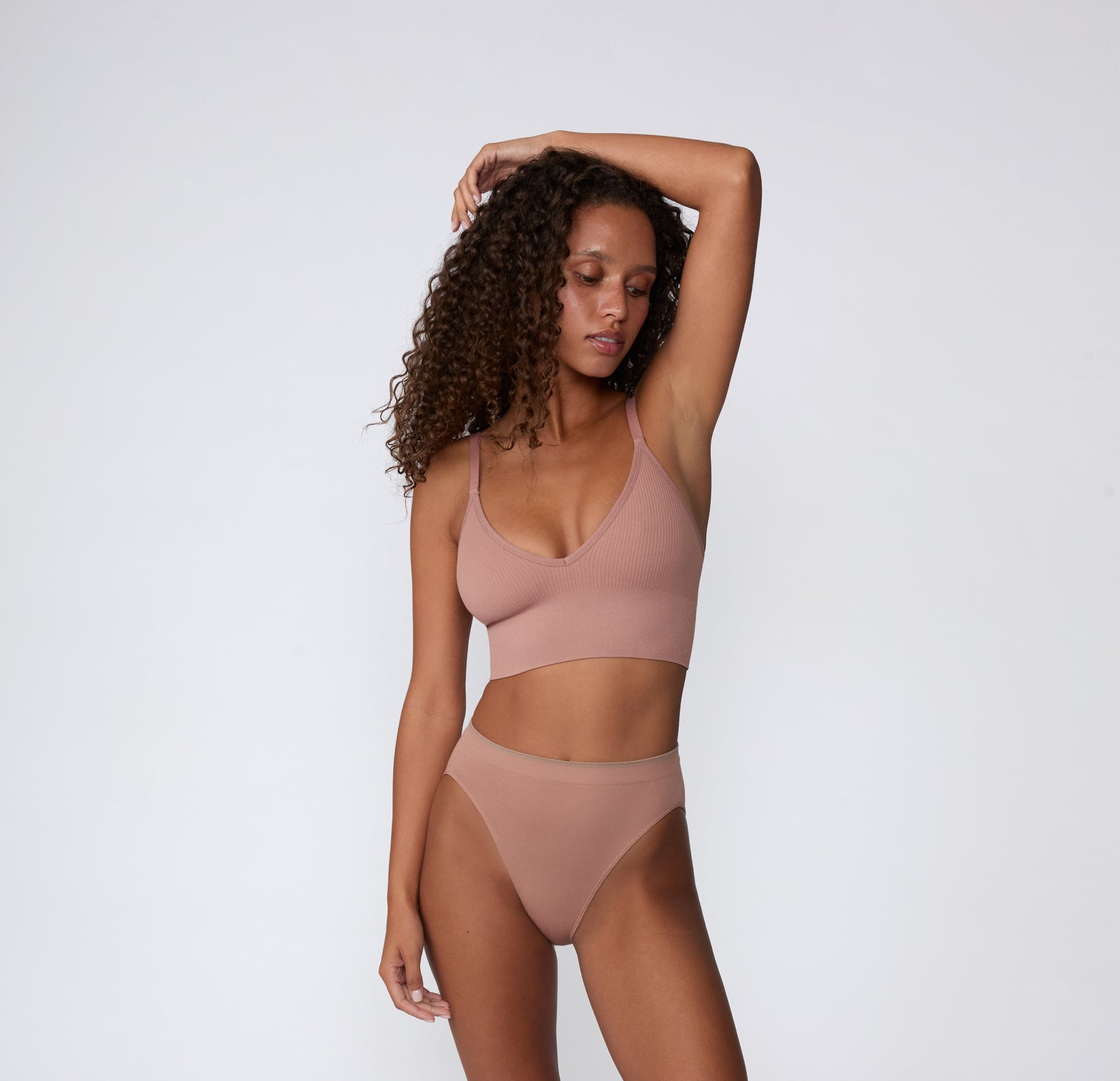 On a light studio backdrop, a full-body front view shows a model wearing the Ribbed Triangle Bralette with matching underwear in Plum, emphasizing the ribbed texture and wireless design.