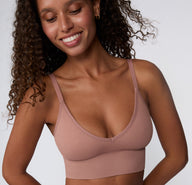 On a light studio backdrop, a close-up front view shows a model wearing the Ribbed Triangle Bralette in Plum, focusing on the triangle shape, ribbed fabric, and smooth underband.