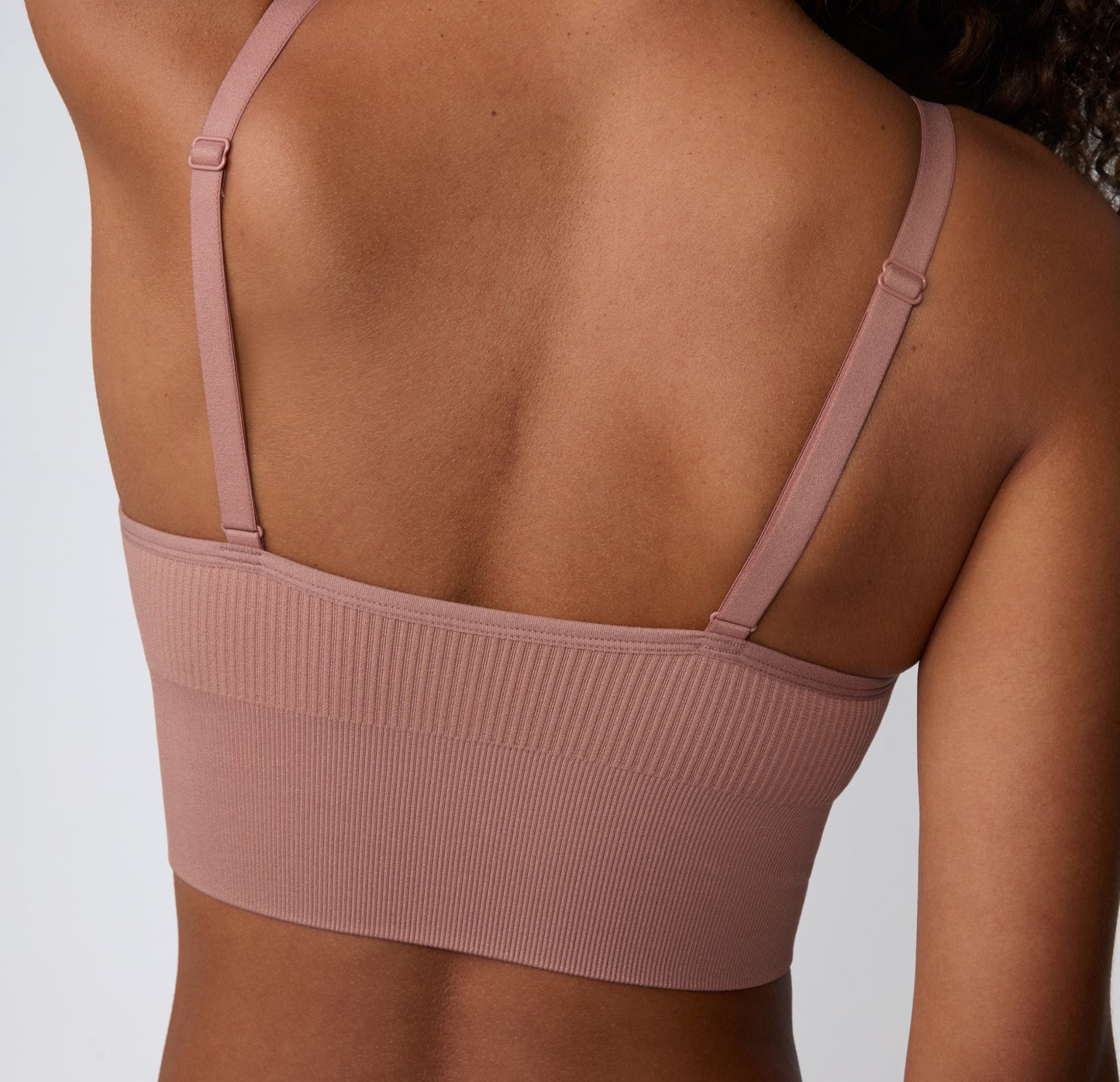 On a light studio backdrop, a back view shows a model wearing the Ribbed Triangle Bralette in Plum, featuring the straight back, adjustable straps, and ribbed construction.