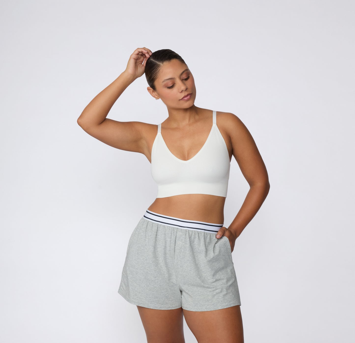 On a light studio backdrop, a full-body front view shows a model wearing the Ribbed Triangle Bralette in White styled with lounge shorts, emphasizing the ribbed texture and wireless design.