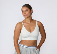 On a light studio backdrop, a three-quarter front view shows a model wearing the Ribbed Triangle Bralette in White with lounge shorts, highlighting the triangle neckline, ribbed construction, and thin straps.