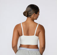On a light studio backdrop, a back view shows a model wearing the Ribbed Triangle Bralette in White, featuring the straight back, adjustable straps, and smooth ribbed construction.