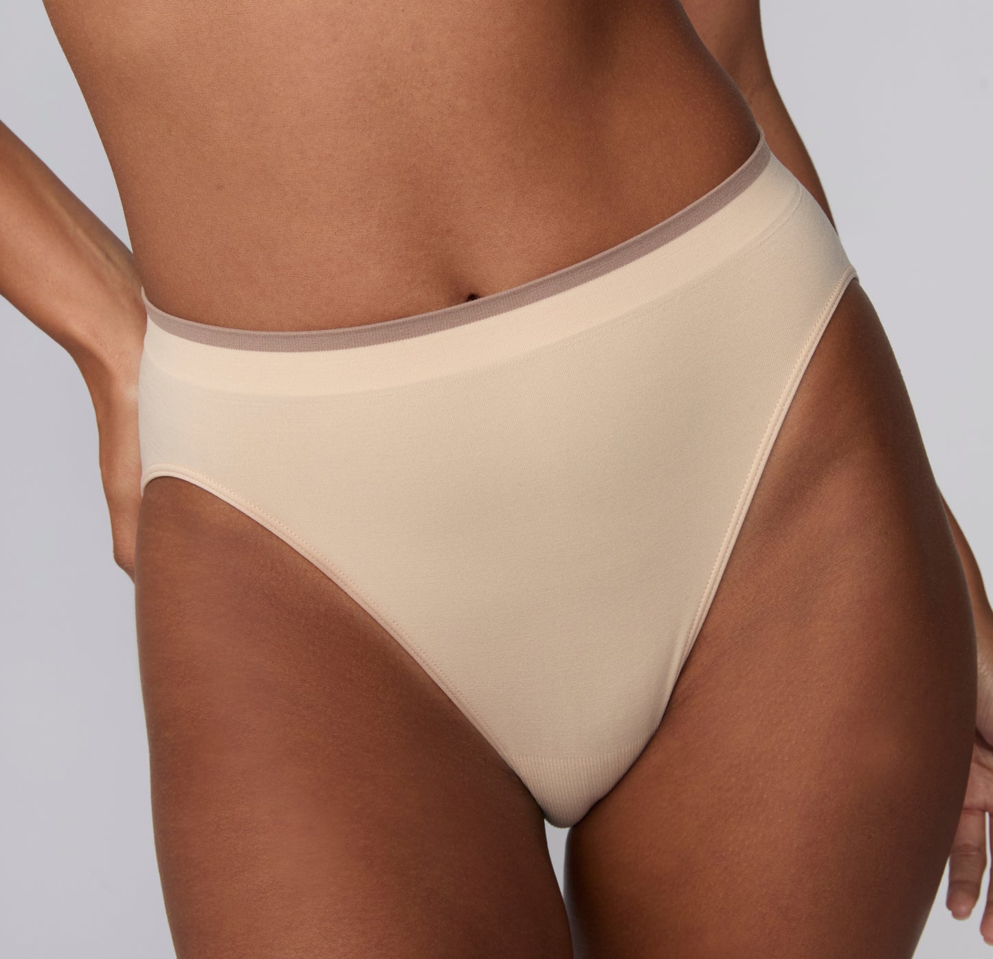 On a light gray studio backdrop, a close-up of Courtney wearing the Smooth Seamless underwear in Beige shows the smooth microfiber fabric and low-rise waistband with subtle contrast trim.