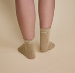 Close up of a model wearing the Quarter Crew Socks in the color Tarragon. The back of the left sock says "Stay" and the back of the right sock says "Wilde".