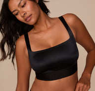 Close-up of Victoria in the Stretch Satin Square Neck Bralette in Black, looking down to the side. The soft shine and fit of the bralette are emphasized.