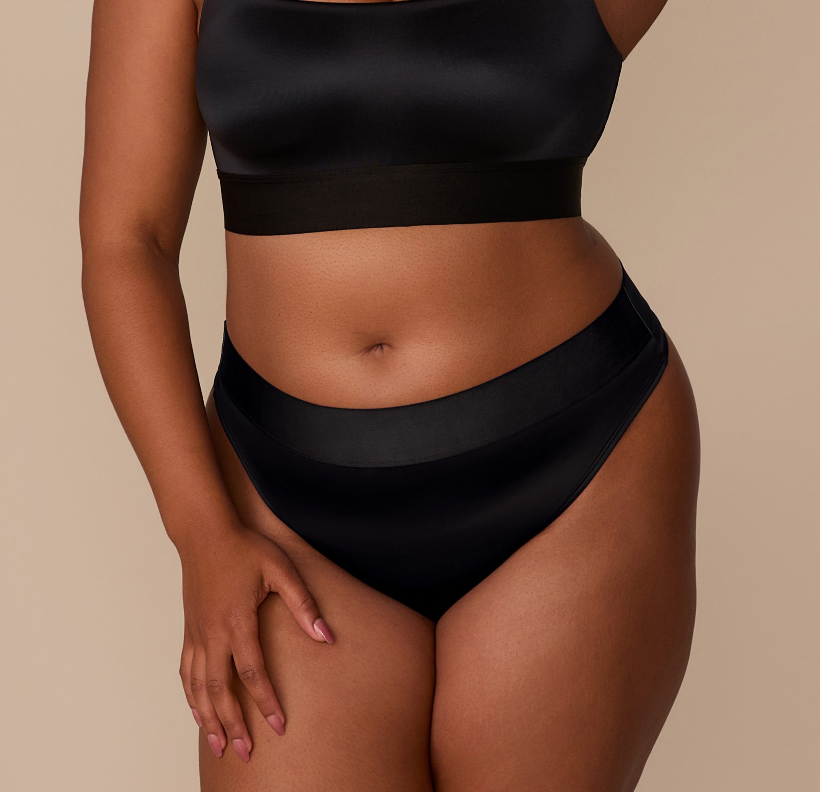 Close-up of Zarria wearing the Stretch Satin Highwaist Thong in Black. The image highlights the smooth waistband and soft satin finish at the front. sizing: Zarria wears size XL