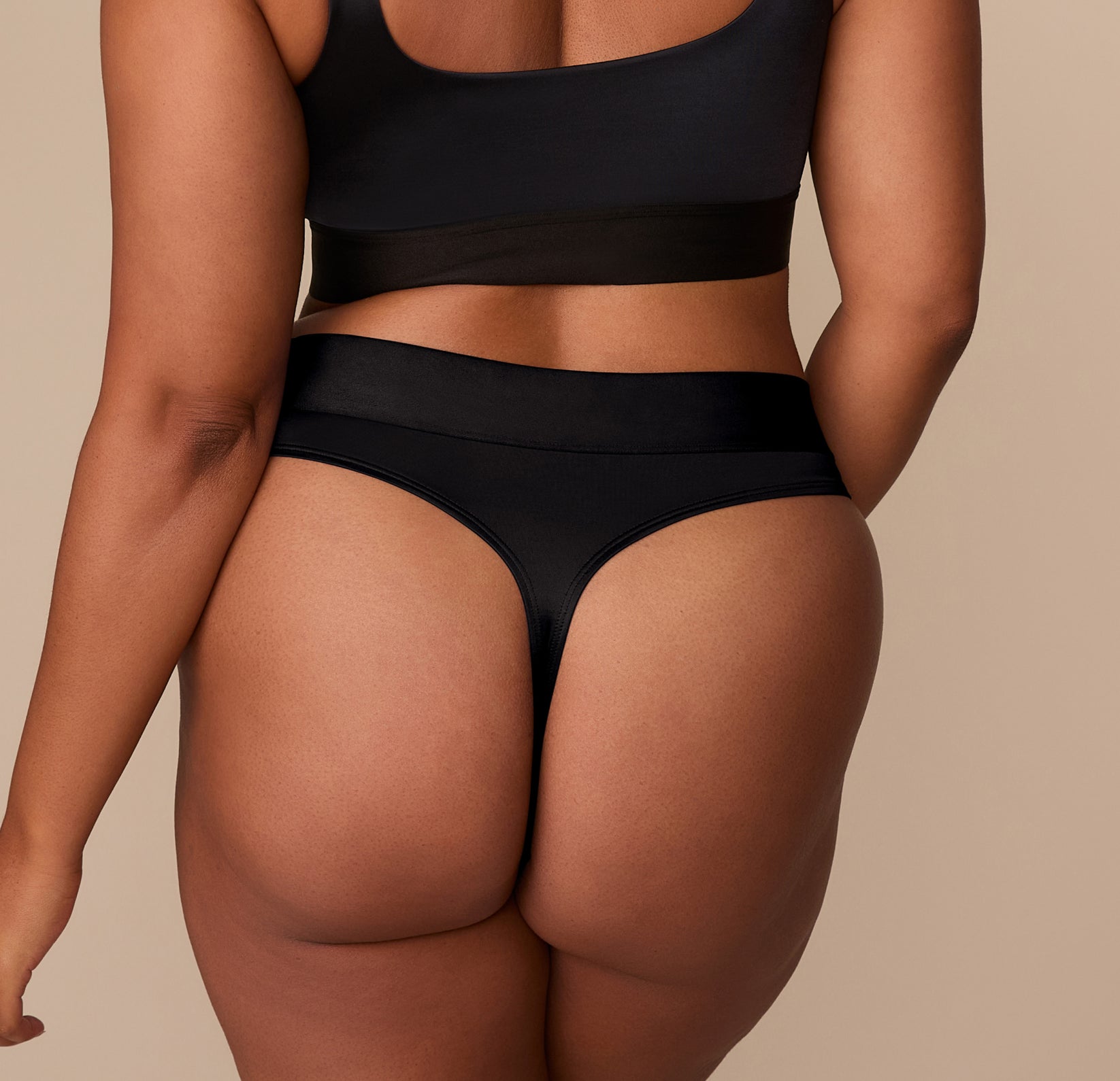 Back view of Zarria wearing the Stretch Satin Highwaist Thong in Black, showing the thong cut and high-rise fit.