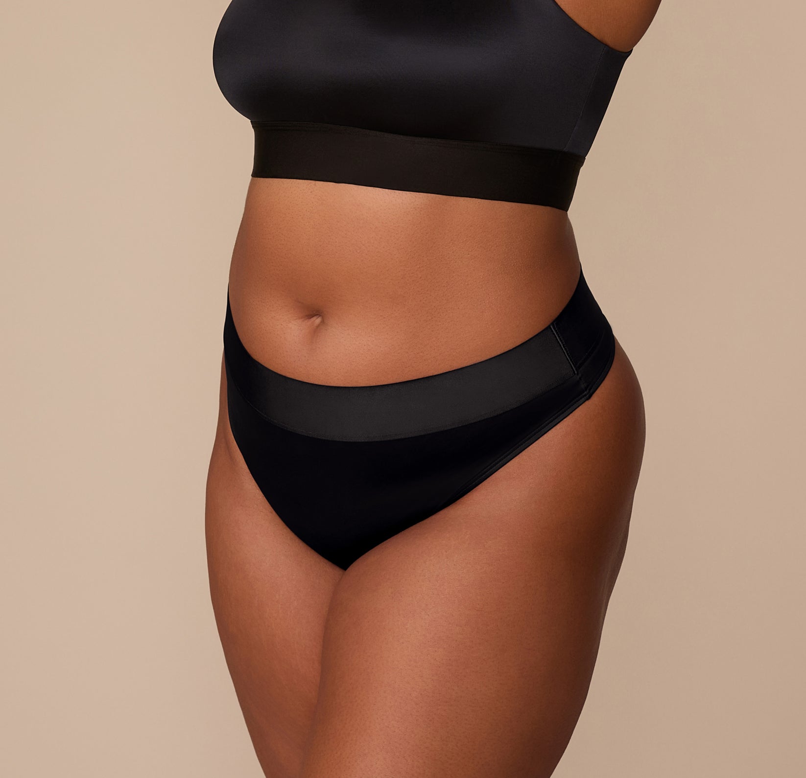 Side view of Zarria in the Stretch Satin Highwaist Thong in Black, showcasing the curve-hugging silhouette and silky texture.