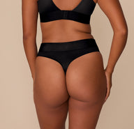 Back view of Victoria wearing the Stretch Satin Highwaist Thong in Black, paired with the Triangle Bralette. The image focuses on the satin thong back and supportive waistband.