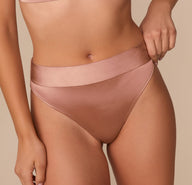 Close-up of Alexis adjusting the waistband of the Stretch Satin Highwaist Thong in Champagne, emphasizing the soft texture and stretch.