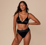 Full front view of Victoria in the Stretch Satin Triangle Bralette and coordinating Stretch Satin Highwaist Thong in Black, with hands on hip and relaxed expression.