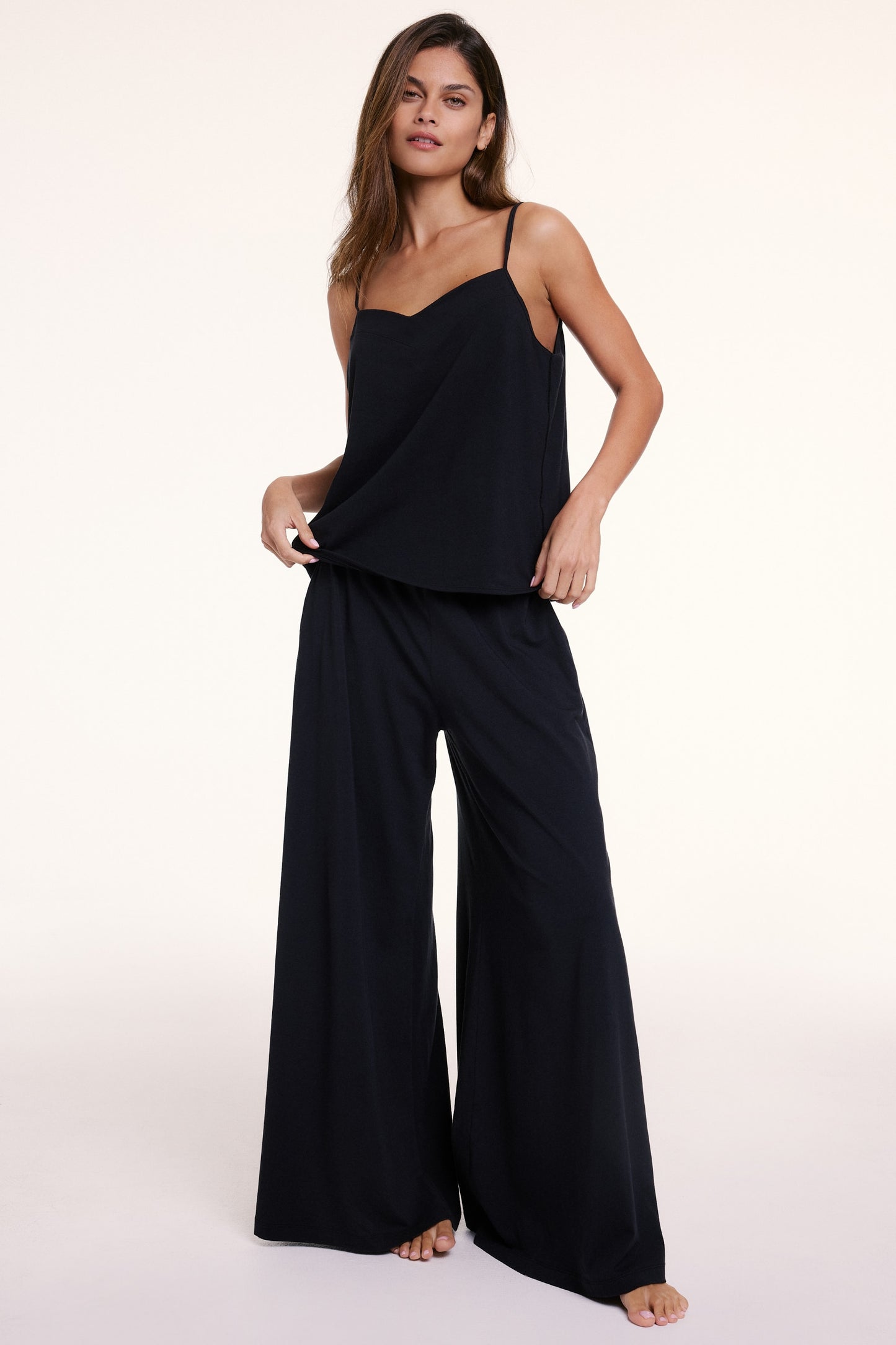 In a studio with a neutral backdrop, Sunday wears the Sunday Pima Cami Pant Set in Black, featuring a lightweight camisole with thin adjustable straps and a relaxed fit, paired with wide-leg pants made from soft, breathable fabric for all-day comfort.