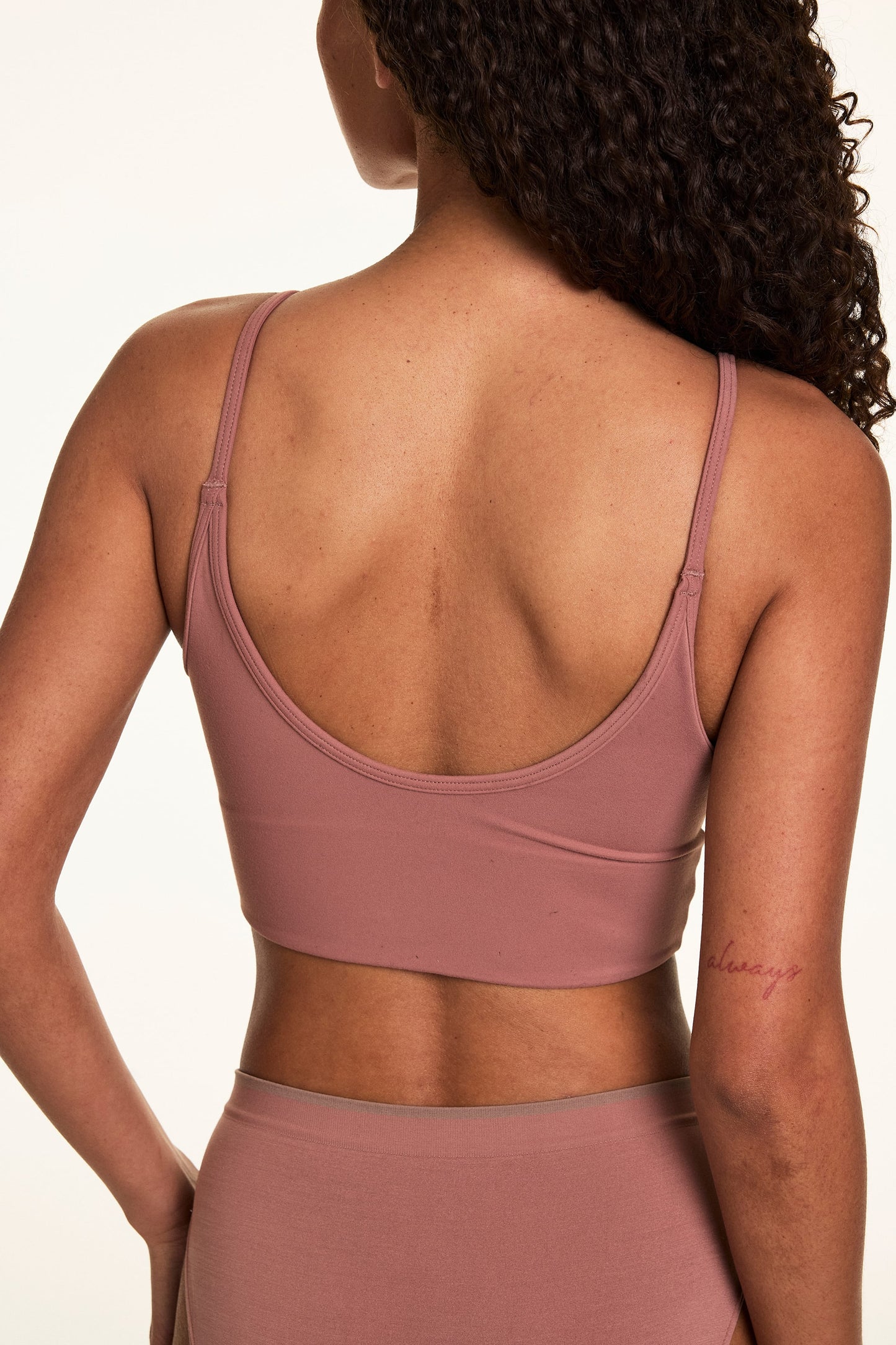 Back view on a light studio backdrop of Courtney wearing the Whipped Knit Scoop Bralette in Plum with matching underwear. The bralette features adjustable straps, a scoop back, and soft knit fabric.