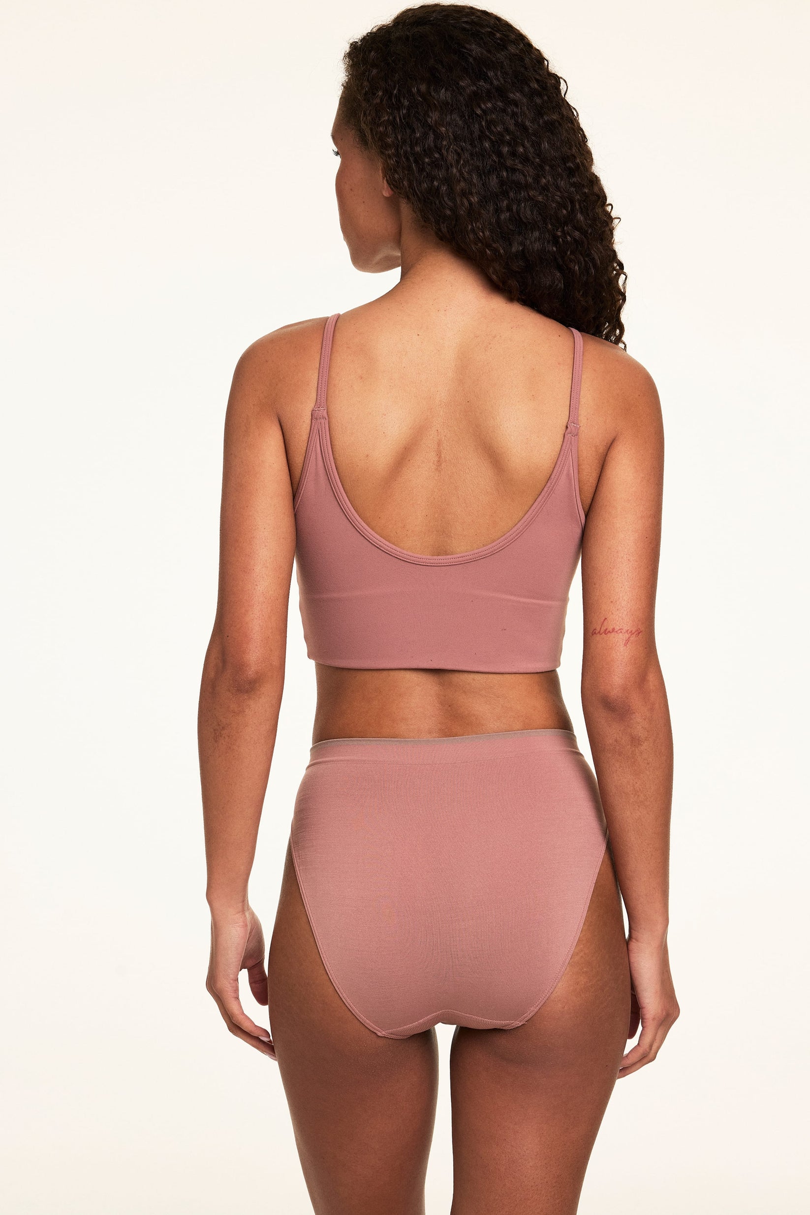 Back view on a light studio backdrop of Courtney wearing the Whipped Knit Scoop Bralette in Plum with matching underwear. The longline bralette features a smooth scoop-back silhouette and thin adjustable straps.