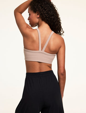 Back view on a light studio backdrop of Courtney wearing the Whipped Knit V-Neck Bralette in Mushroom with black wide-leg lounge pants. The bralette features wide straps, a V-back design, and a smooth longline band.