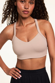 On a light studio backdrop, Courtney wears the Whipped Knit V-Neck Bralette in Mushroom with black lounge pants. The bralette features a soft V-neckline, wide straps, and a smooth longline fit.