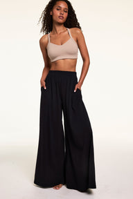 Full-length studio portrait of Courtney wearing the Whipped Knit V-Neck Bralette in Mushroom with black wide-leg lounge pants. The bralette features a soft V-neckline, wide straps, and smooth knit fabric.