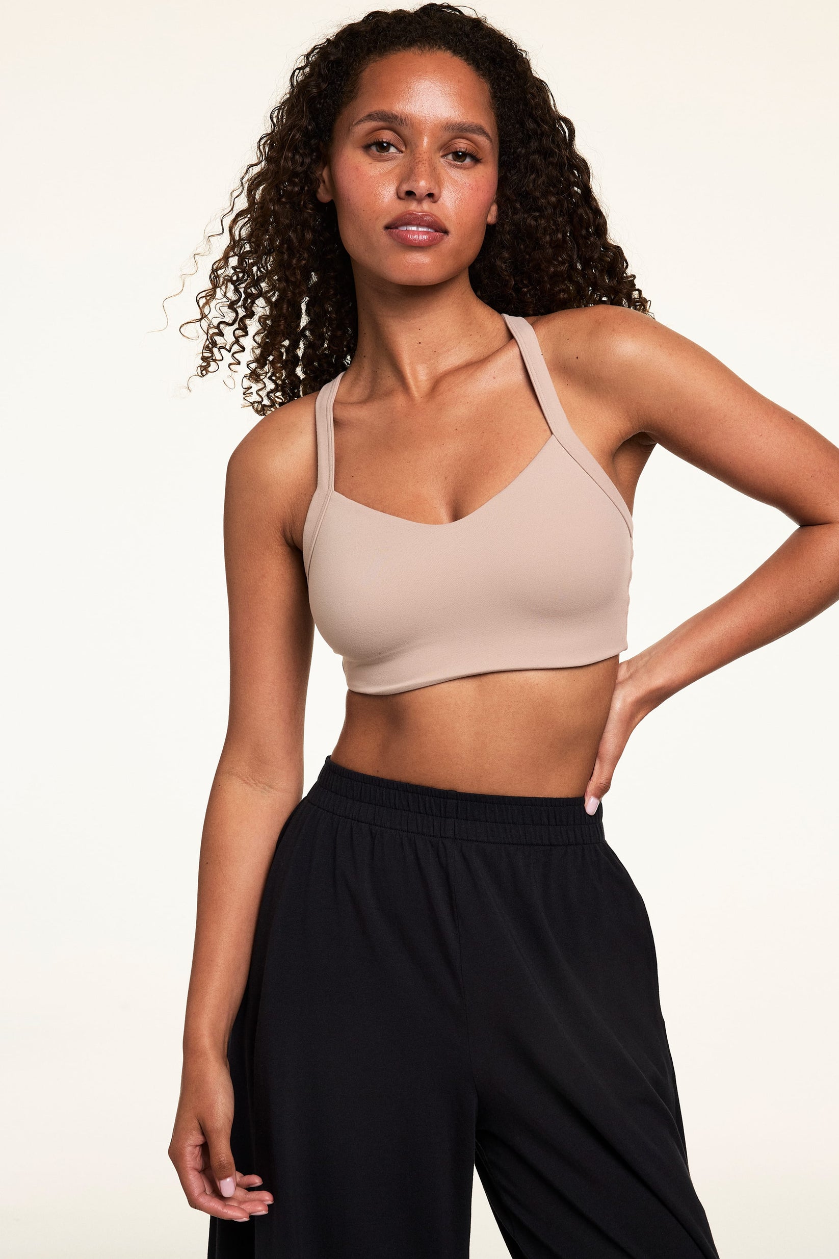 Studio portrait of Courtney wearing the Whipped Knit V-Neck Bralette in Mushroom with black wide-leg lounge pants. The bralette features a smooth V-neckline, wide straps, and a soft longline fit