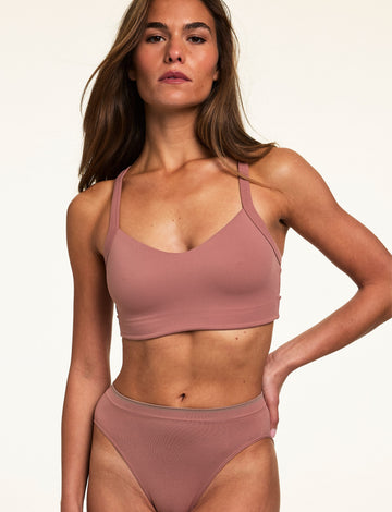 On a light studio backdrop, Gianna wears the Whipped Knit V-Neck Bralette in Plum with matching high-rise underwear. The bralette features a soft V-neckline, wide straps, and smooth knit fabric.