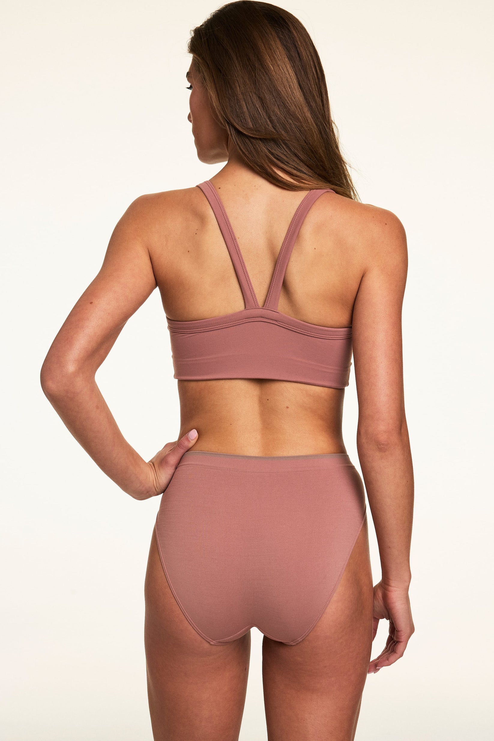 Back view on a light studio backdrop of Gianna wearing the Whipped Knit V-Neck Bralette in Plum with matching high-rise underwear. The bralette features wide straps, a V-back design, and a smooth longline band.