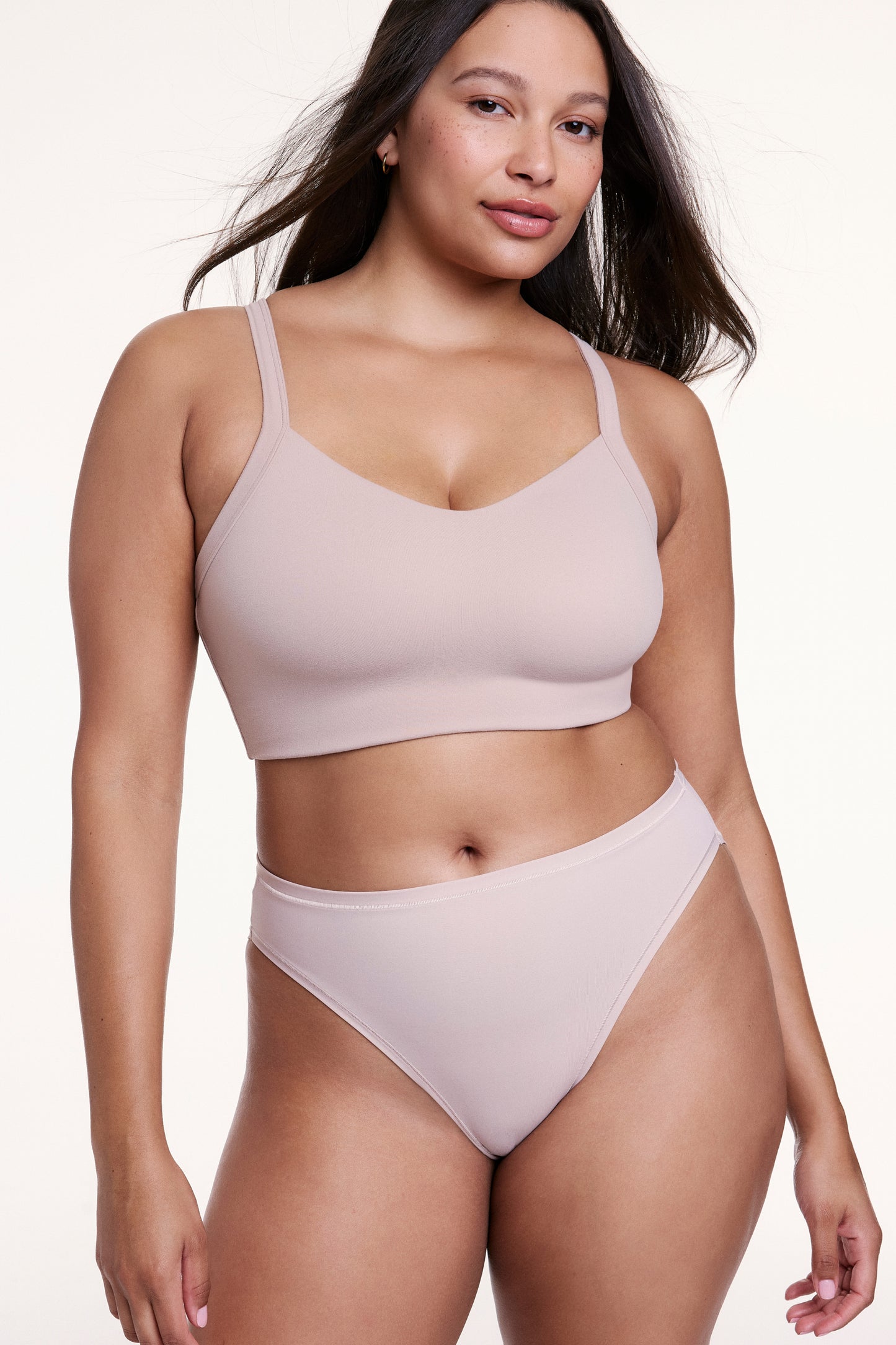 Against a neutral studio backdrop, Alana wears the Whipped Knit V-Neck Bralette in Mushroom with matching underwear, showing the V-neckline, smooth knit fabric, and wireless design for comfortable support. sizing: Alana wears size Large