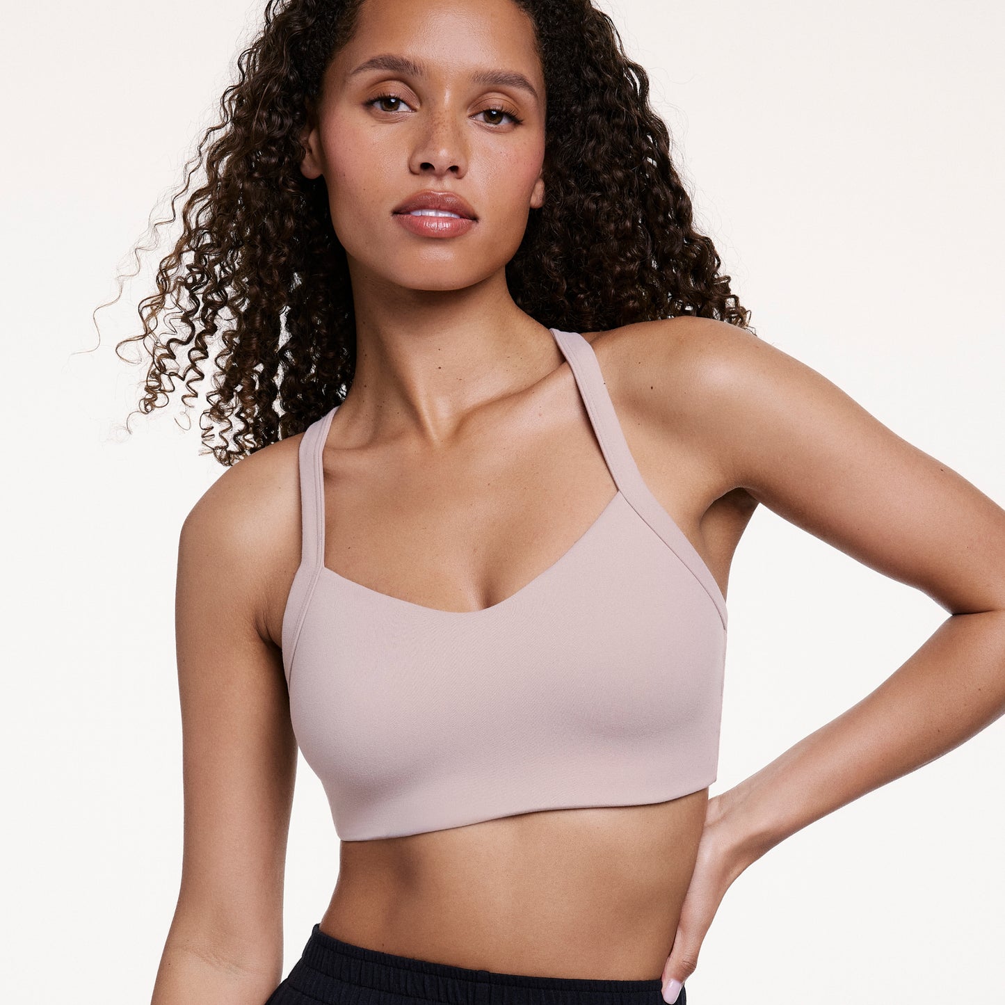 Against a neutral studio backdrop, Courtney wears the Whipped Knit V-Neck Bralette in Mushroom, showing the V-neckline, smooth knit fabric, and wide straps. Her hand rests at her hip.