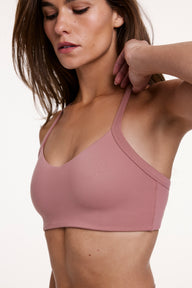 In a close-up studio shot, Gianna wears the Whipped Knit V-Neck Bralette in Plum, adjusting the strap. The bralette features a V-neckline, textured knit fabric, and wireless design for comfortable support.