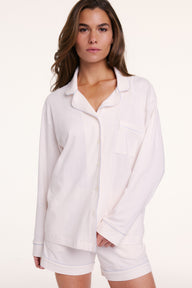 On a neutral backdrop, Gianna wears the Perfect Pima Pajama Long Sleeve Shirt in Ivory with matching shorts. The shirt is buttoned and features a relaxed fit, long sleeves, and a chest pocket.