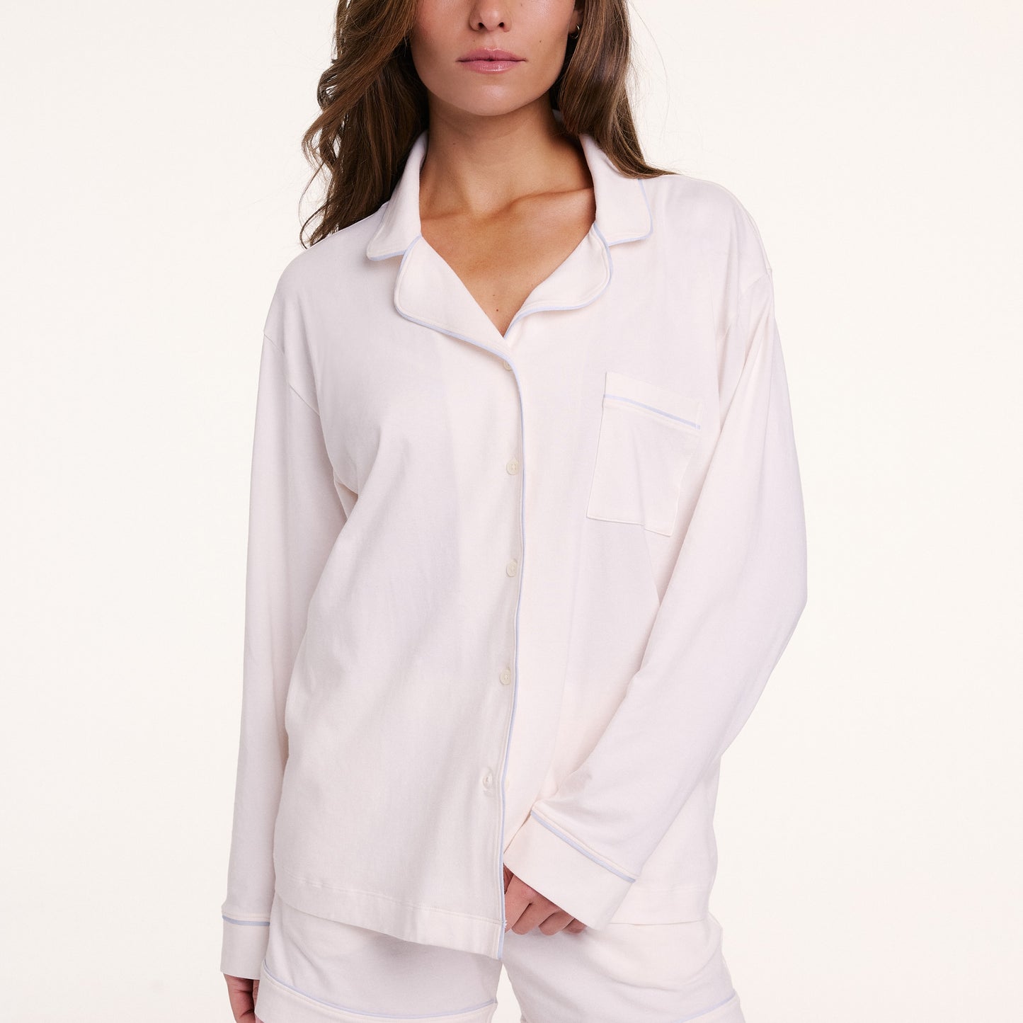 In a studio setting, Gianna wears the Perfect Pima Pajama Long Sleeve Shirt in Ivory with matching shorts. The shirt is buttoned, showing the soft drape, long sleeves, and chest pocket.