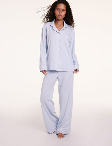 In a studio setting, Courtney wears the Perfect Pima Pajama Long Sleeve Shirt in Soft Blue with matching pants, featuring a relaxed fit, button-front design, and long sleeves.