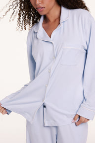 In a studio setting, Courtney wears the Perfect Pima Pajama Long Sleeve Shirt in Soft Blue with matching pants, featuring a relaxed fit, button-front design, and long sleeves.