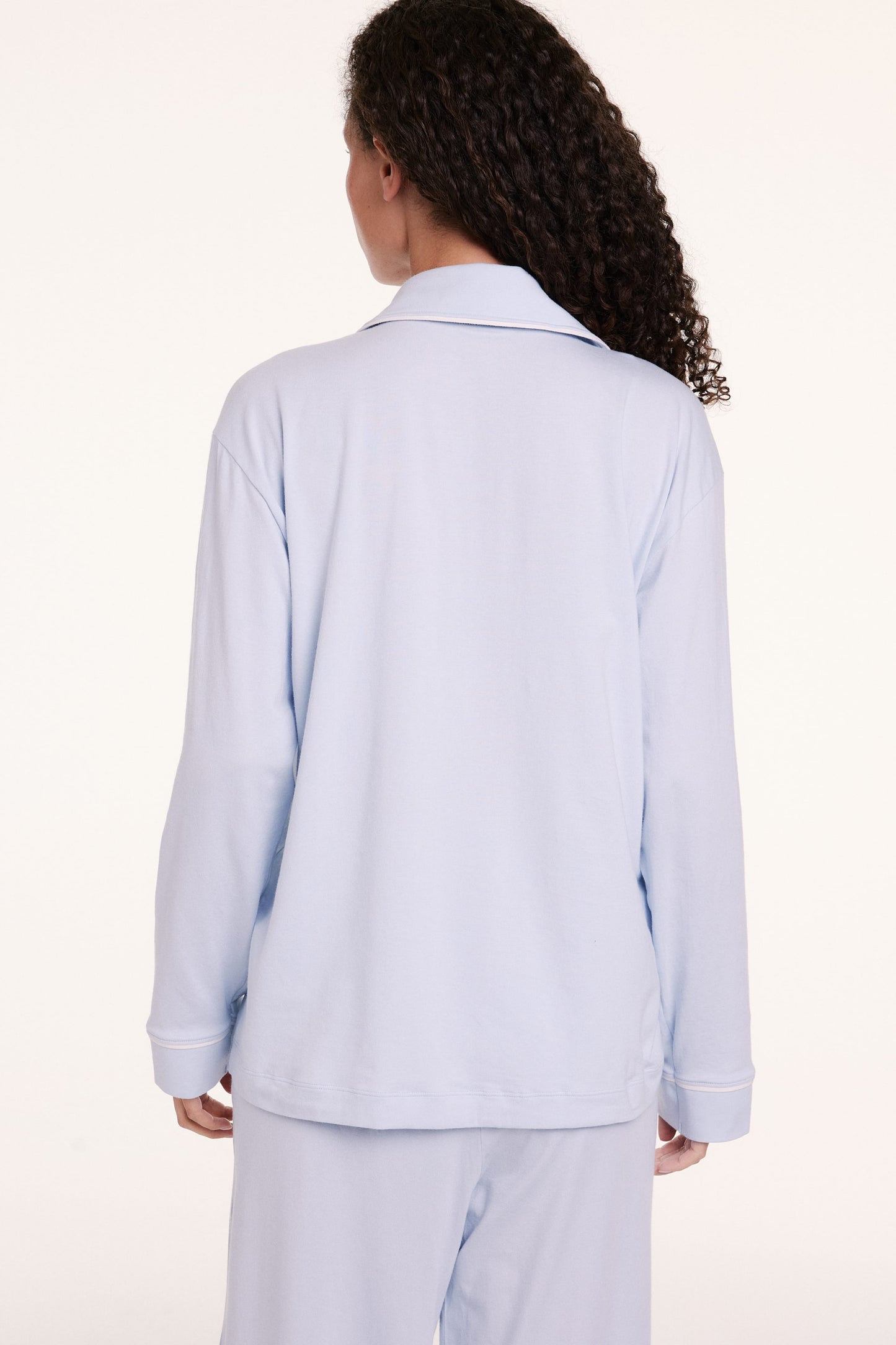 In a studio setting, Courtney wears the Perfect Pima Pajama Long Sleeve Shirt in Soft Blue, shown in a close-up highlighting the soft fabric, buttons, and chest pocket detail.