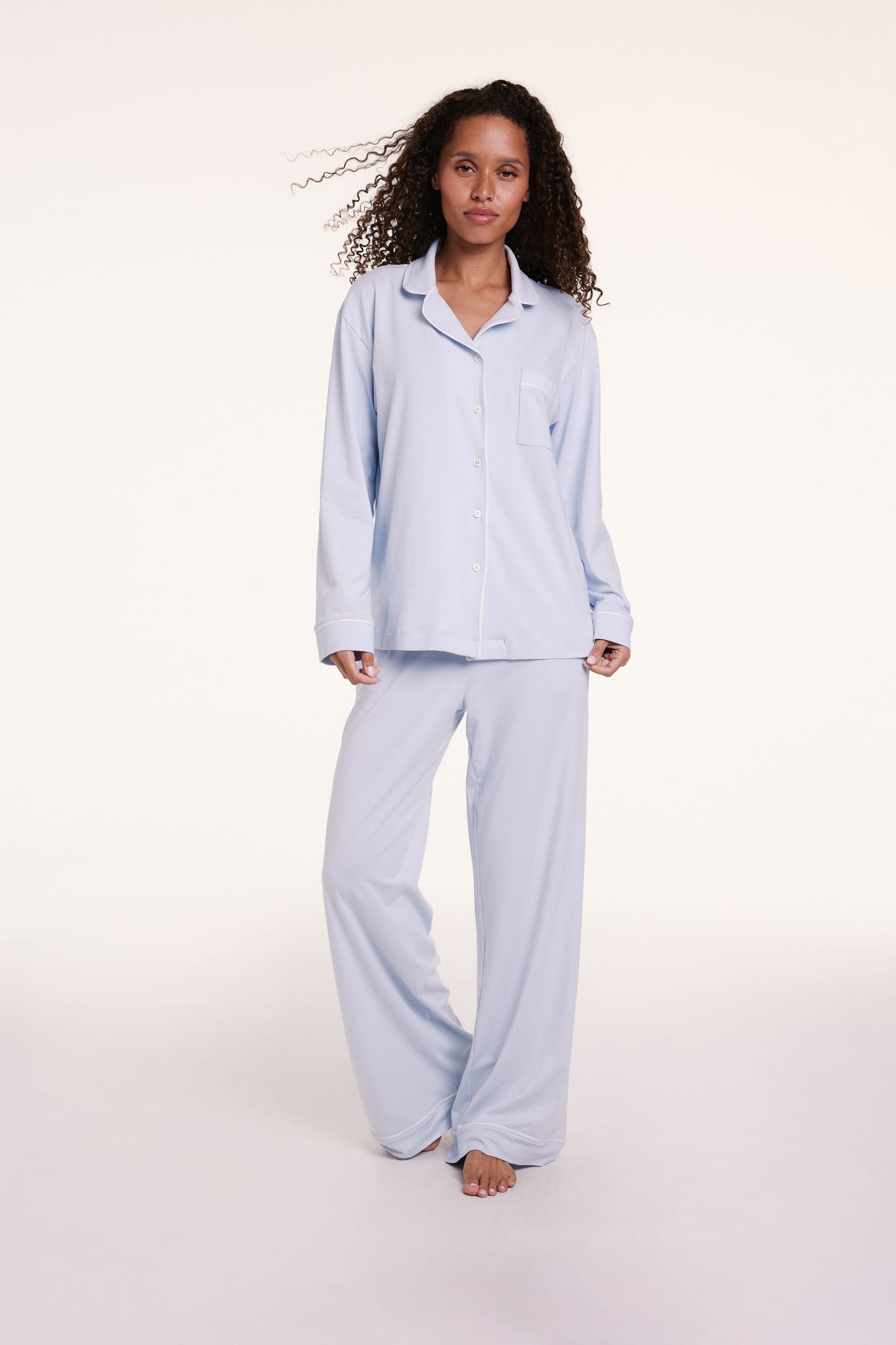 On a light studio backdrop, Courtney wears the Perfect Pima Pajama Set in Soft Blue, featuring a long-sleeve button-down top with a relaxed fit and matching wide-leg pants. Linni wears size Small
