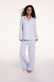 On a light studio backdrop, Courtney wears the Perfect Pima Pajama Set in Soft Blue, featuring a long-sleeve button-down top with a relaxed fit and matching wide-leg pants. Linni wears size Small
