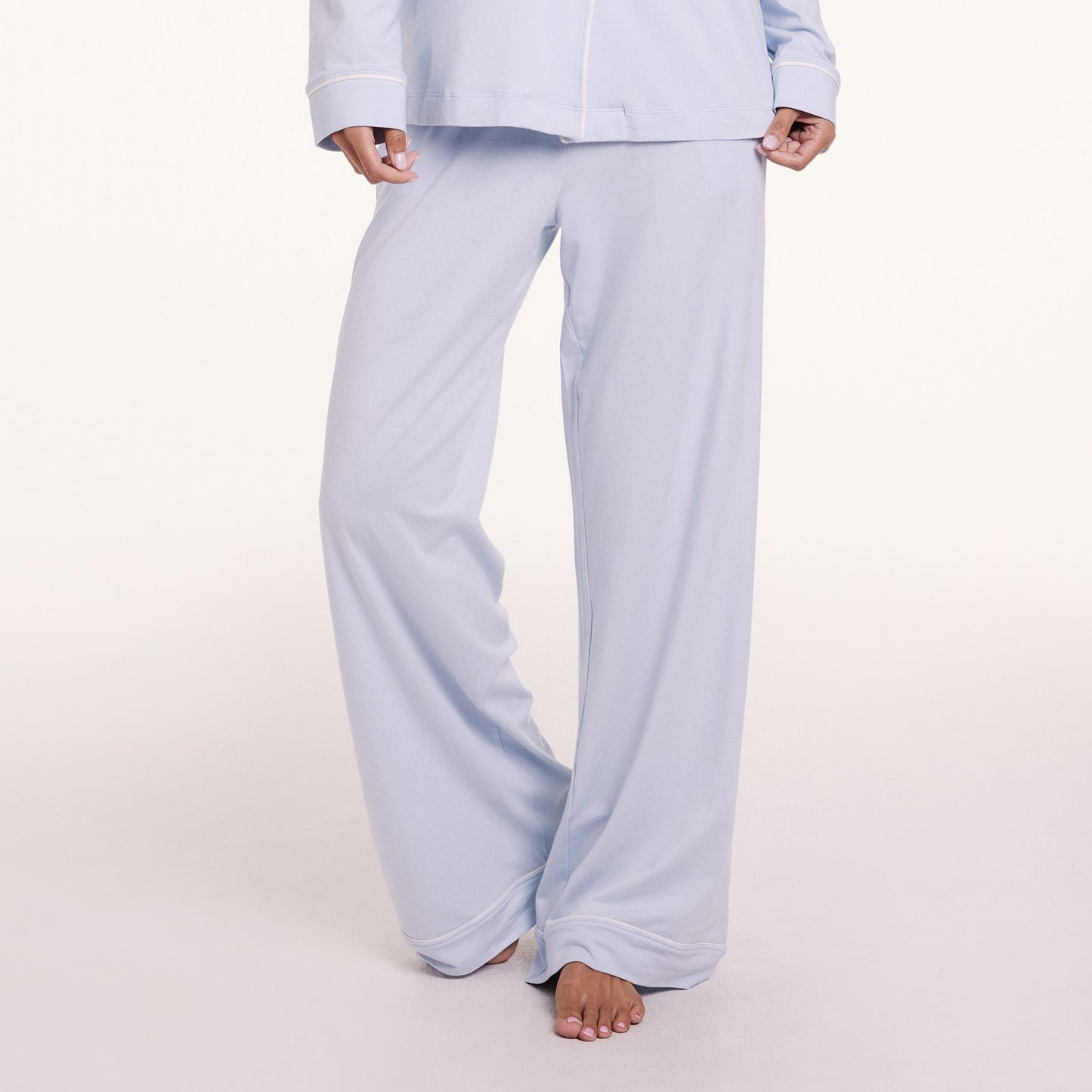 On a light studio backdrop, Courtney wears the Perfect Pima Pajama Pants in Soft Blue, featuring a wide-leg fit and smooth, lightweight fabric.