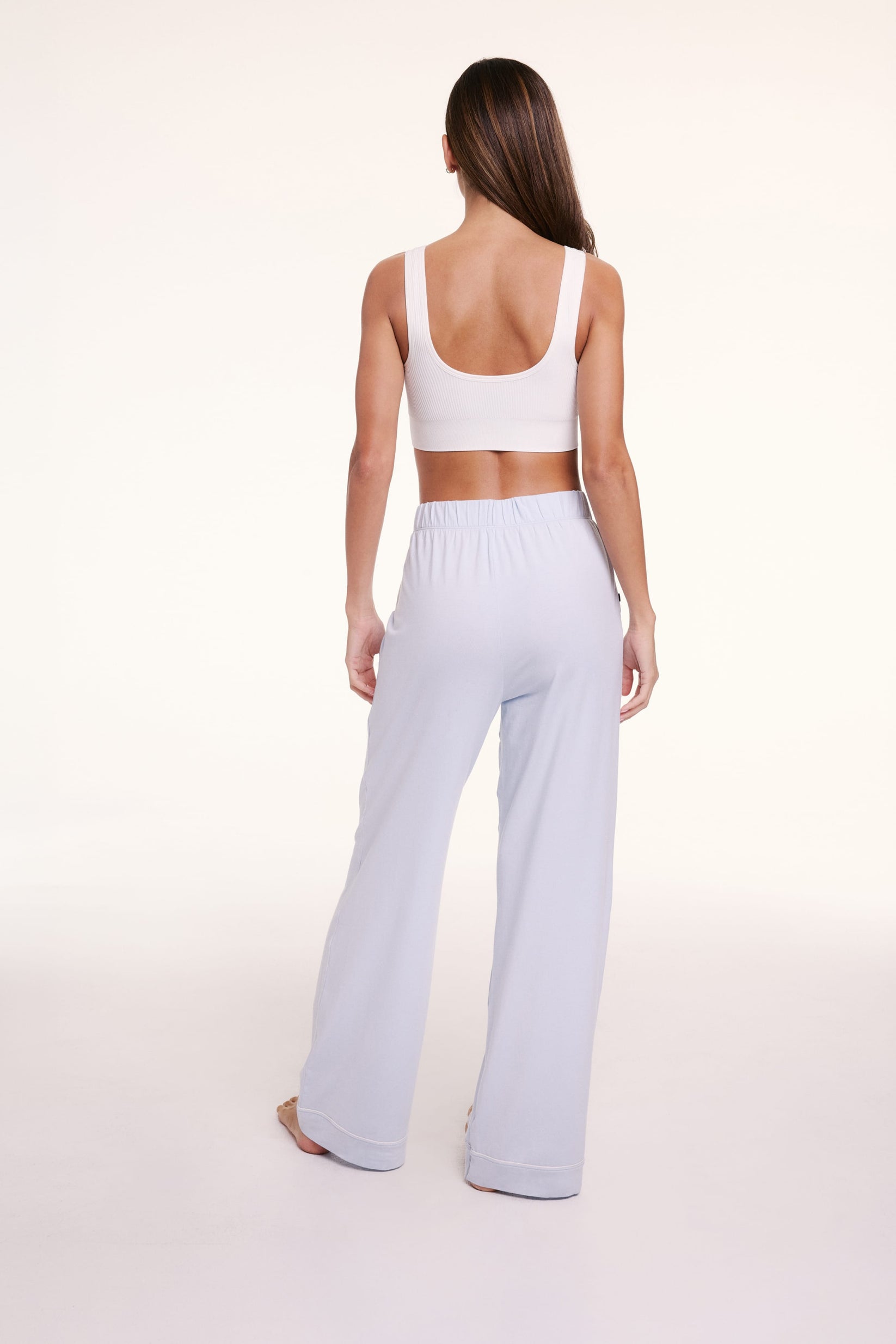 On a light studio backdrop, Linni wears the Perfect Pima Pajama Pants in Soft Blue, shown from the back with a relaxed, wide-leg silhouette.