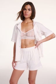 On a neutral backdrop, Gianna wears the Perfect Pima Pajama Shirt in Ivory with matching shorts, styled open to show a mesh bralette. The set features a relaxed fit, button front, and contrast piping details. sizing: Gianna wears size Small