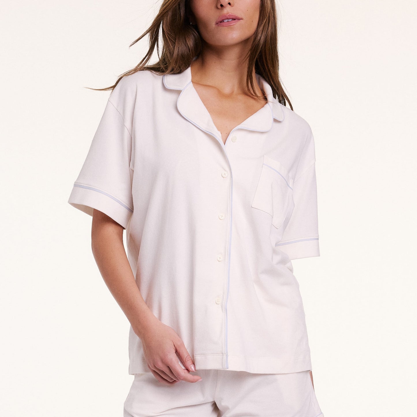 On a neutral backdrop, Gianna wears the Perfect Pima Pajama Shirt in Ivory with matching shorts. The shirt is buttoned, showing the soft drape, chest pocket, and contrast piping along the collar and placket.