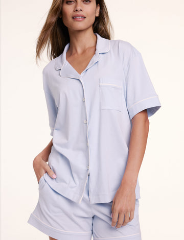 In a studio setting, Linni wears the Perfect Pima Pajama Short Sleeve Shirt in Soft Blue with matching shorts, featuring a button-front design, chest pocket, and soft, breathable fabric.
