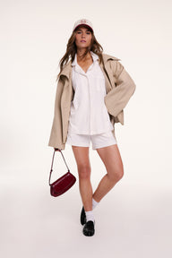 On a light studio backdrop, Gianna wears the Perfect Pima Pajama Shorts Set in Ivory styled with a jacket, cap, and loafers, featuring the button-down top and relaxed shorts.