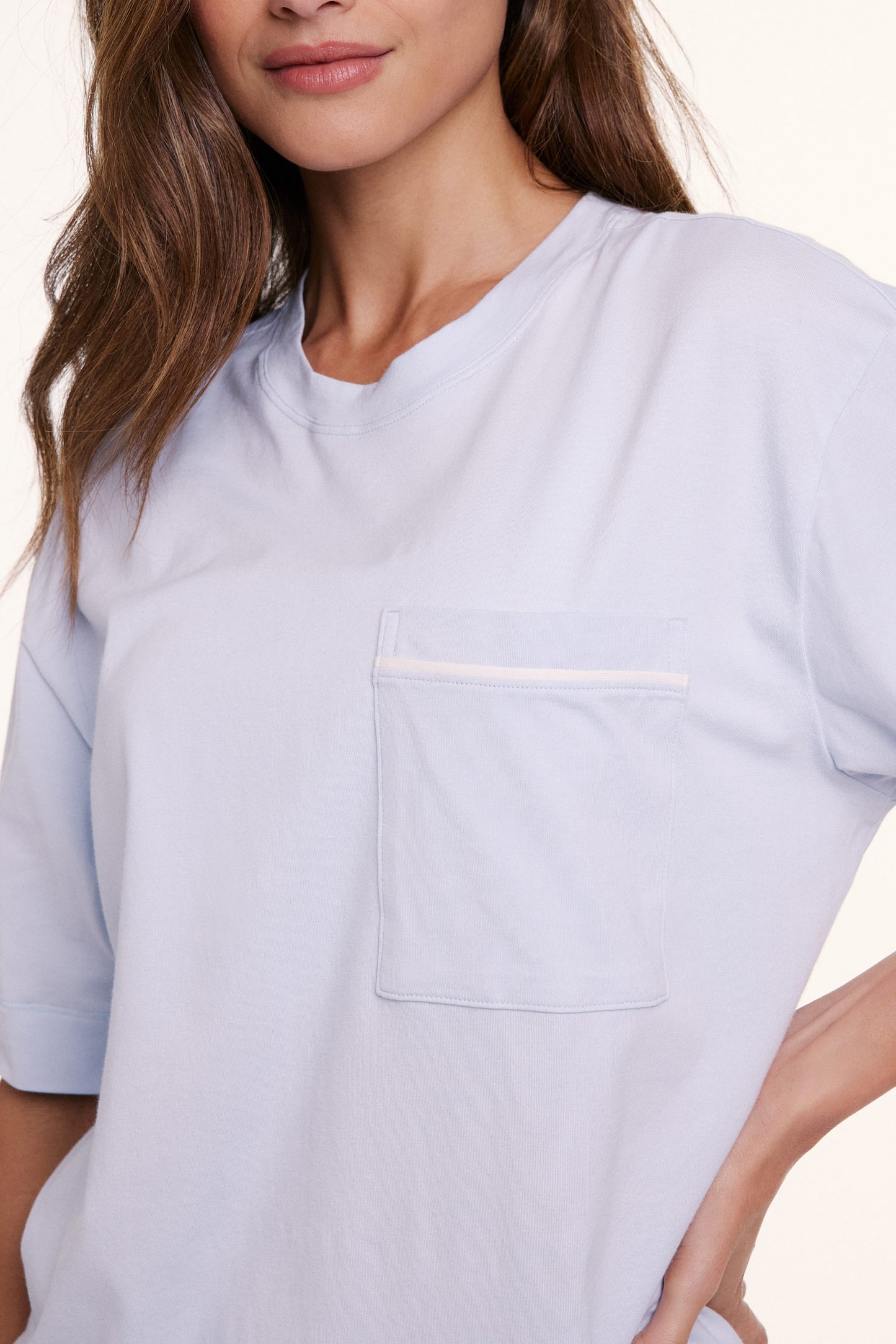 In a studio setting, Linni wears the Perfect Pima Pajama Tee in Soft Blue, shown in a close-up of the chest pocket and smooth, breathable fabric.