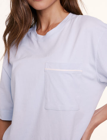 In a studio setting, Linni wears the Perfect Pima Pajama Tee in Soft Blue, shown in a close-up of the chest pocket and smooth, breathable fabric.