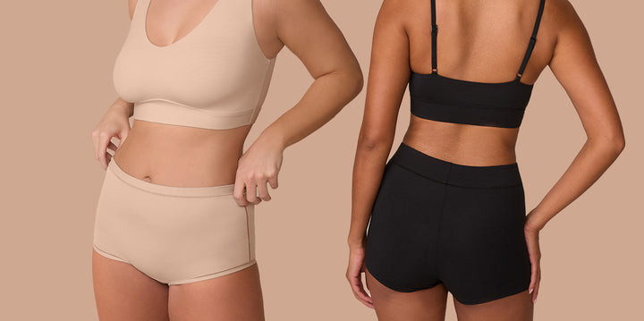 Two models stand side by side wearing the Bliss Bralette and Bliss Scoop Bralette in Beige and Black. They both wear the matching Bliss Boyshort to make a monochrome set. The left model showcases the deep V-neck and wireless support of the Bliss Bralette in Beige, with its smooth, elastic-free design. The right model faces away from the camera, highlighting the adjustable straps and scoop back of the Bliss Scoop Bralette in Black, as well as the full coverage and stay-put comfort of the Bliss Boyshort.