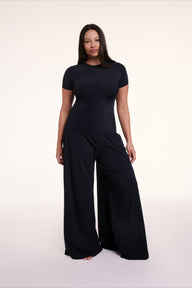 In a studio setting, Alana wears the Sunday Pima Pant in Black with a matching short sleeve top, showing the relaxed, wide-leg silhouette and soft, drapey fabric. Alana wears size Large