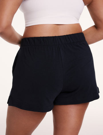On a white studio backdrop, Alana wears the Sunday Pima Short in Black, showing the relaxed fit, elastic waistband, and smooth, lightweight fabric from the back.